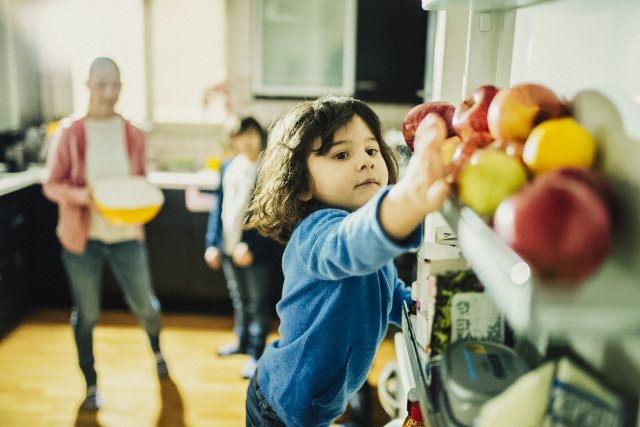 Young person reaches into fridge for an apple